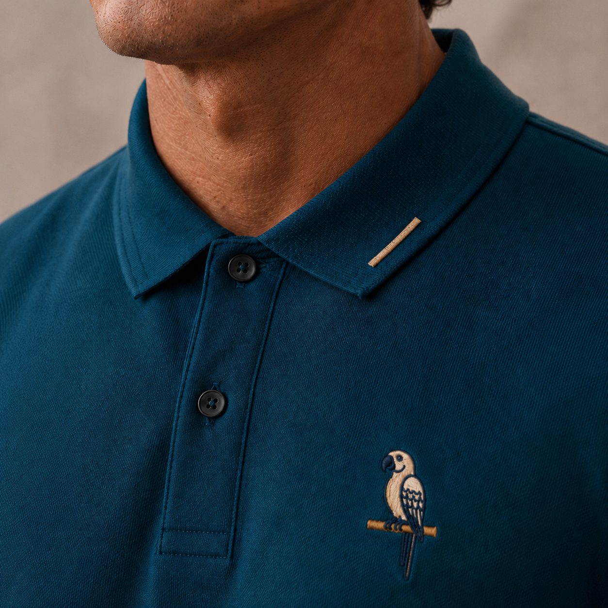 Close-up of the collar tip showing a brass horizontal perch-bar embroidery detail with the parrot emblem on the chest visible below